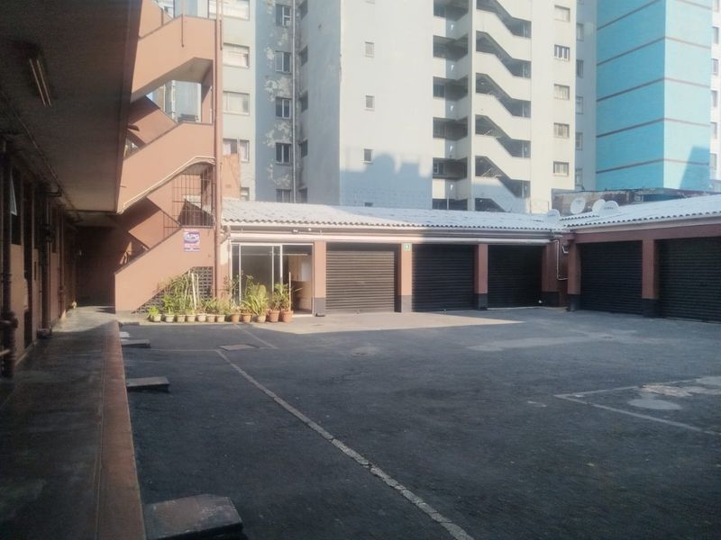 A paved courtyard area featuring multiple garage units with roller shutter doors and an external staircase leading to upper levels.