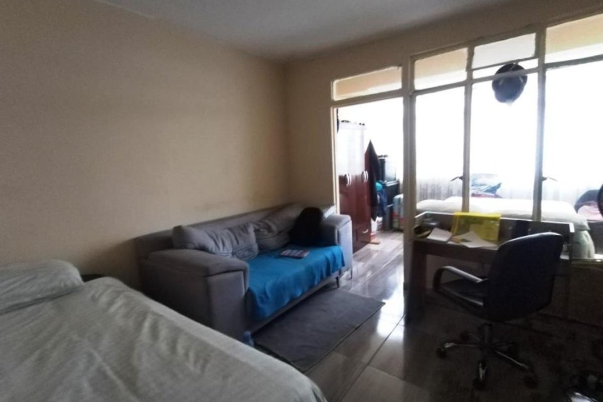 A bedroom featuring tiled flooring and a large glass partition wall with a sliding door, providing natural light and a view into the adjacent space.