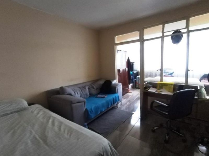 A bedroom featuring tiled flooring and a large glass partition wall with a sliding door, providing natural light and a view into the adjacent space.