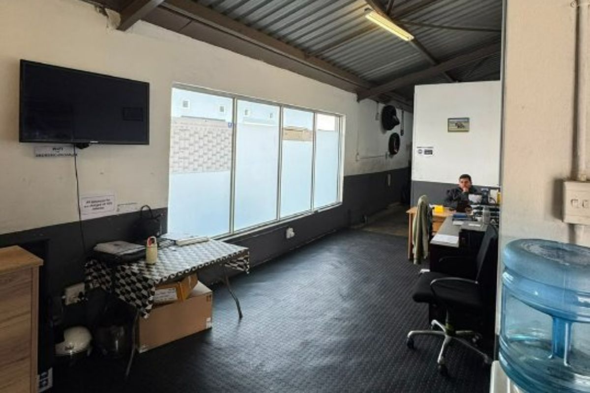 A functional commercial office space featuring exposed metal roofing, large windows for natural light, and durable rubberized flooring.