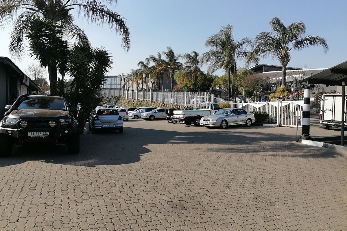 A paved commercial parking area featuring security fencing, gated access, and established palm trees.