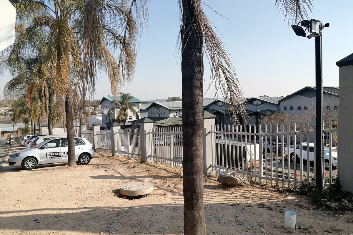 Exterior view of the commercial property frontage featuring metal security fencing, security lighting, and a paved driveway area.