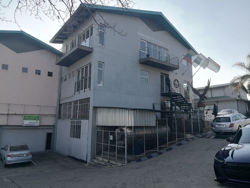 Multi-story commercial building featuring industrial storage tanks, external metal staircases, balconies, and a dedicated warehouse entrance with a roller shutter door.