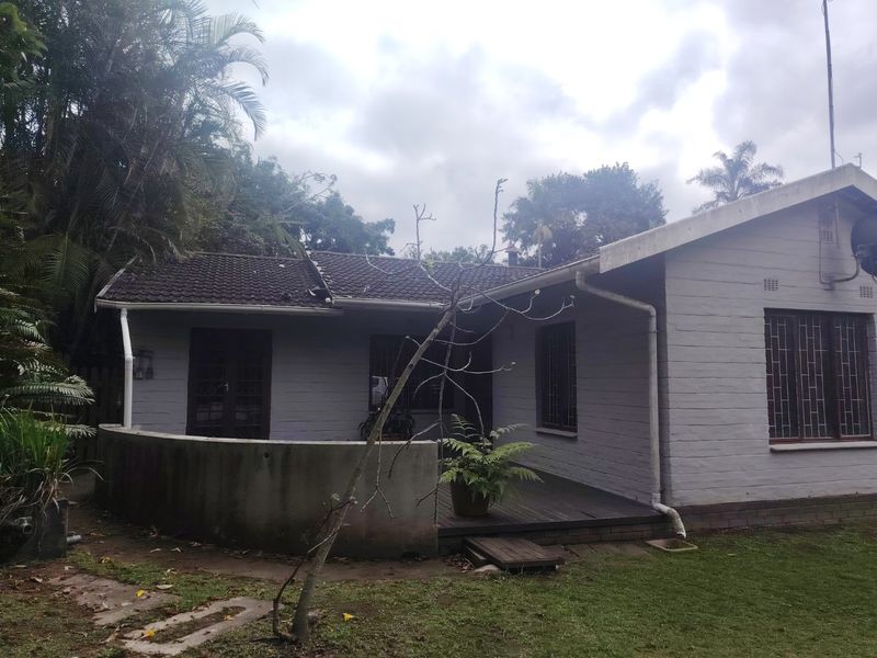 Rear view of a single-story brick house featuring a tiled roof, security bars on windows, and a timber deck area with a concrete retaining wall.