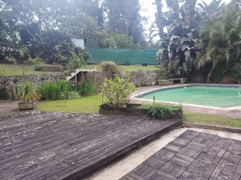 Outdoor pool area featuring a swimming pool, stone retaining wall, and weathered timber decking set within a garden environment.