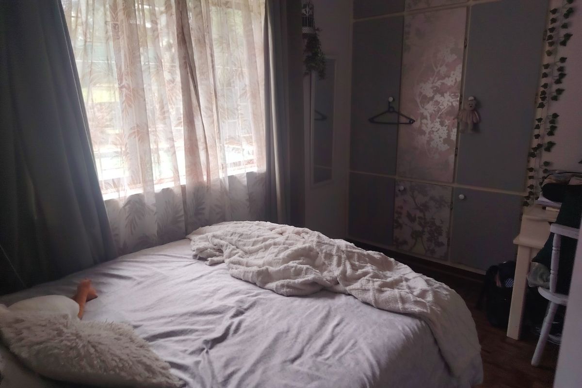 A bedroom featuring built-in cupboards and parquet flooring, offering a functional space with natural light.