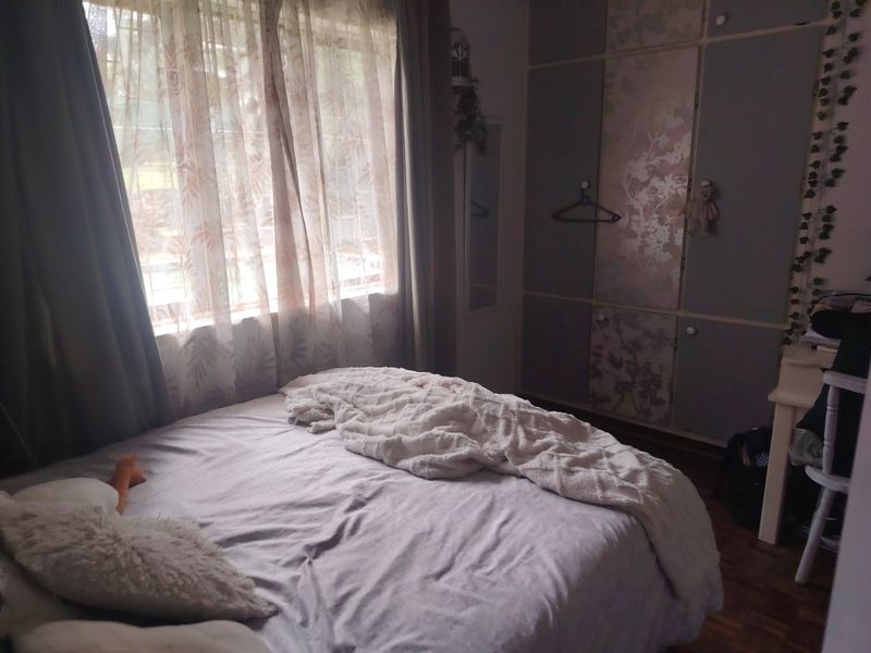 A bedroom featuring built-in cupboards and parquet flooring, offering a functional space with natural light.
