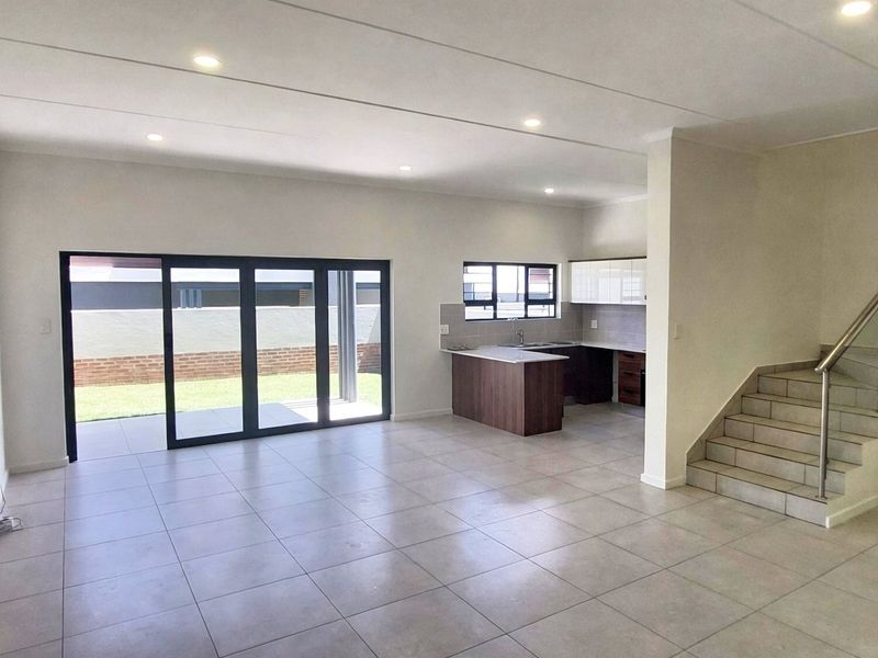 Spacious open-plan living area featuring tiled floors, recessed lighting, a modern kitchen, and large sliding doors opening to a private patio and garden.