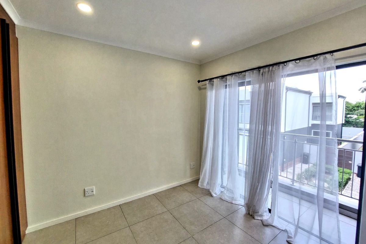 An empty bedroom featuring tiled flooring, recessed lighting, and a sliding glass door leading to a private balcony.