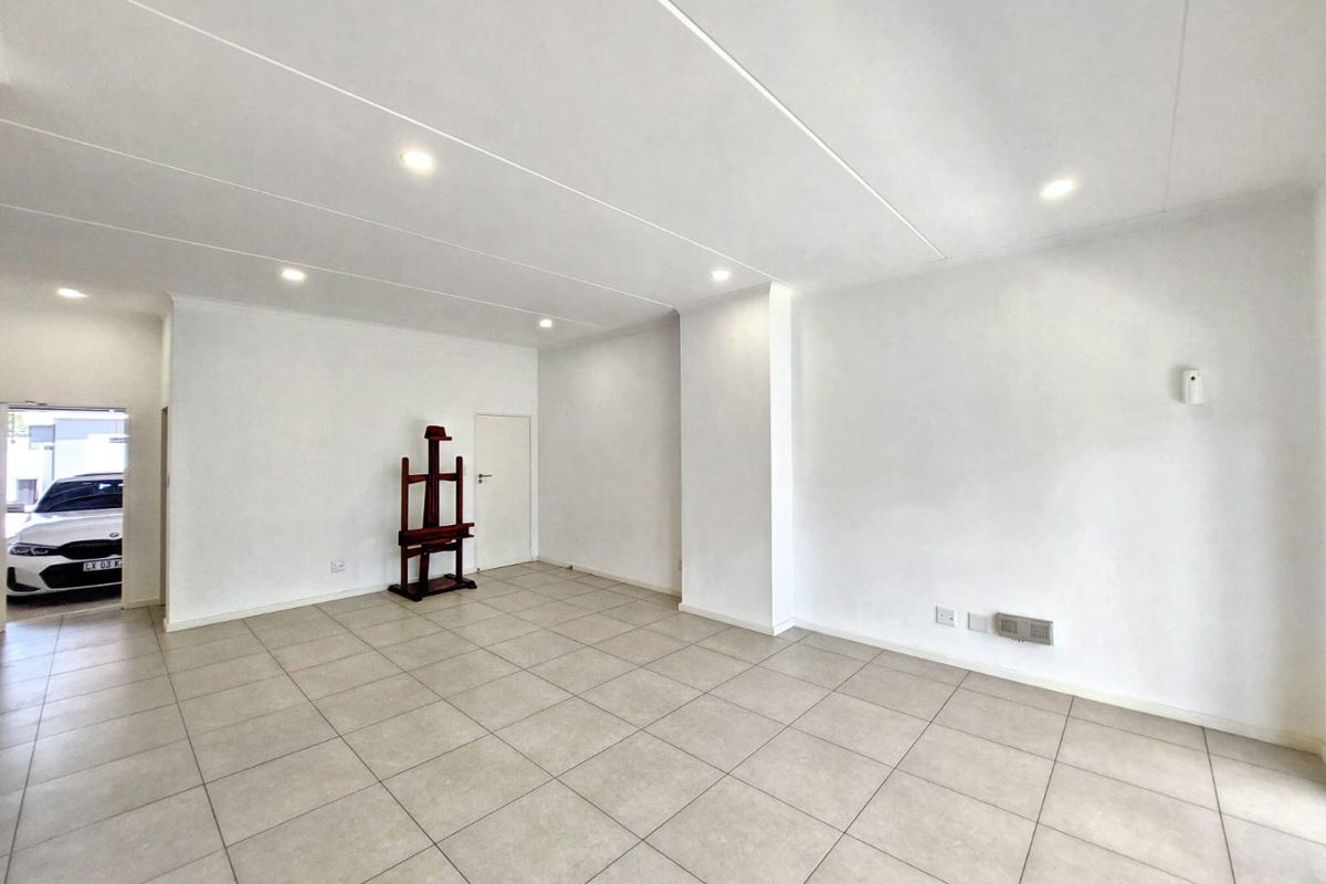 A bright, open-plan living area featuring neutral tiled flooring and recessed downlighting, offering a clean and versatile space ready for furnishing.