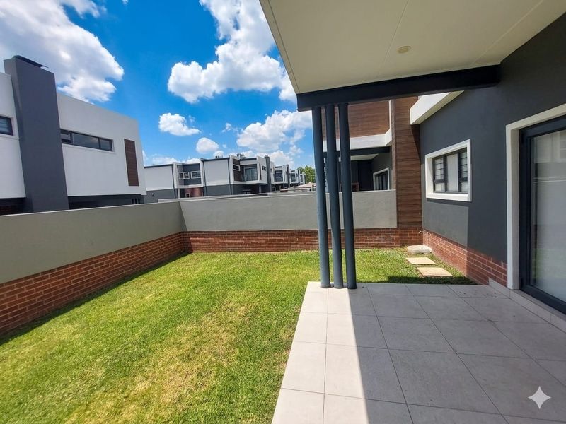 A private rear garden featuring a tiled patio area, neat lawn, and brick boundary walls, providing a clean outdoor space for the townhouse.