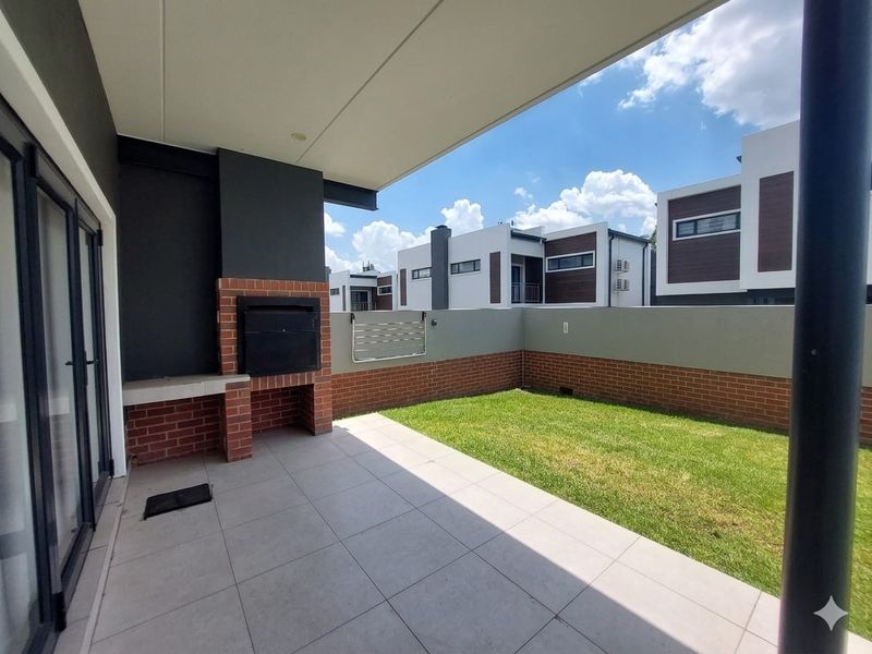 A modern covered patio featuring a built-in brick braai, tiled flooring, and a private garden area, perfect for outdoor entertaining.