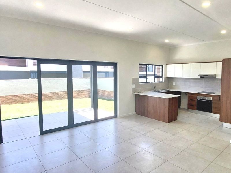 Modern open-plan kitchen and living area featuring tiled floors, sleek cabinetry, built-in appliances, and large sliding doors opening to a private patio and garden.