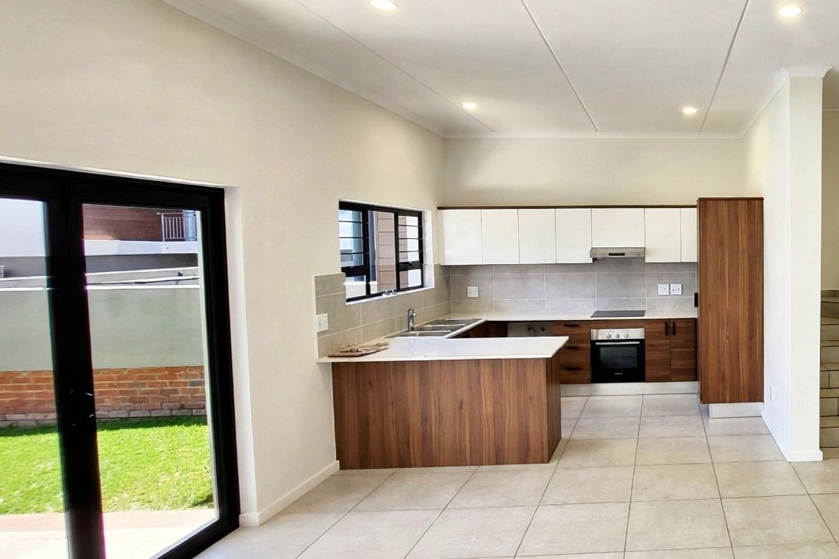 Modern open-plan kitchen featuring sleek wood-tone and white cabinetry, stone countertops, integrated appliances, and direct access to the outdoor garden area.