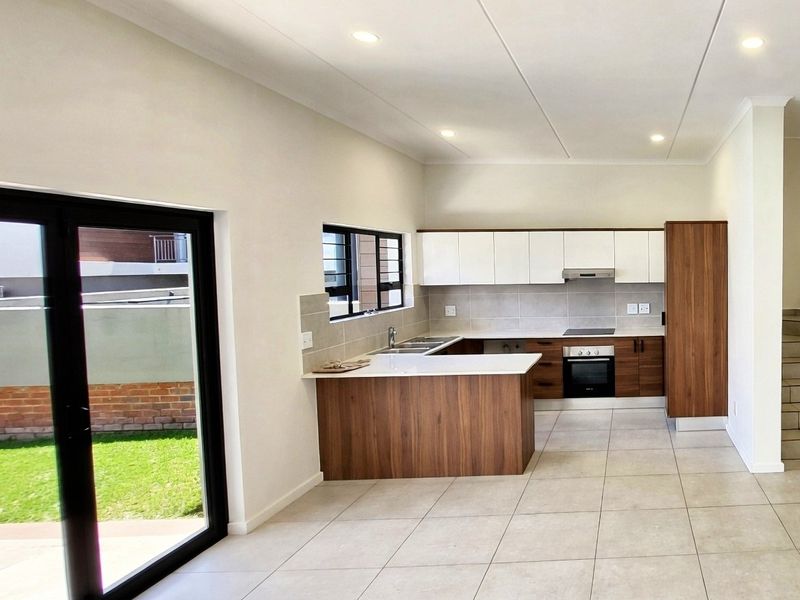 Modern open-plan kitchen featuring sleek wood-tone and white cabinetry, stone countertops, integrated appliances, and direct access to the outdoor garden area.