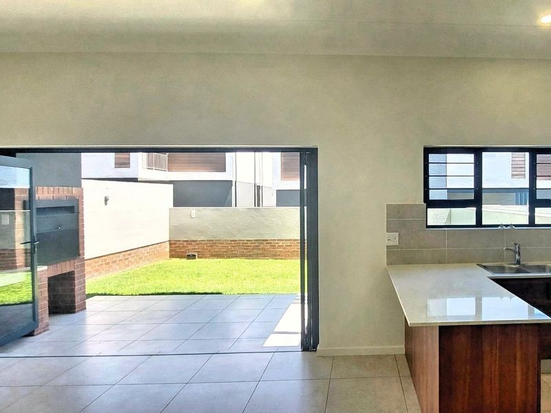 Open plan kitchen area flowing seamlessly through large stacking doors to a tiled patio with a built-in braai and private garden.