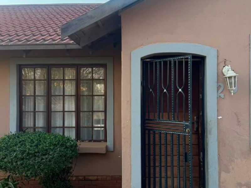 Front entrance of the house featuring a security gate, tiled roof, and timber window frames, showing signs of exterior wear.