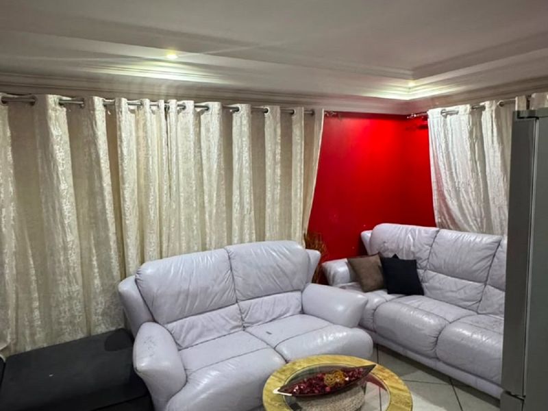 A living room area featuring ceramic floor tiles, a recessed ceiling design, and curtain tracks, providing a functional space for relaxation.