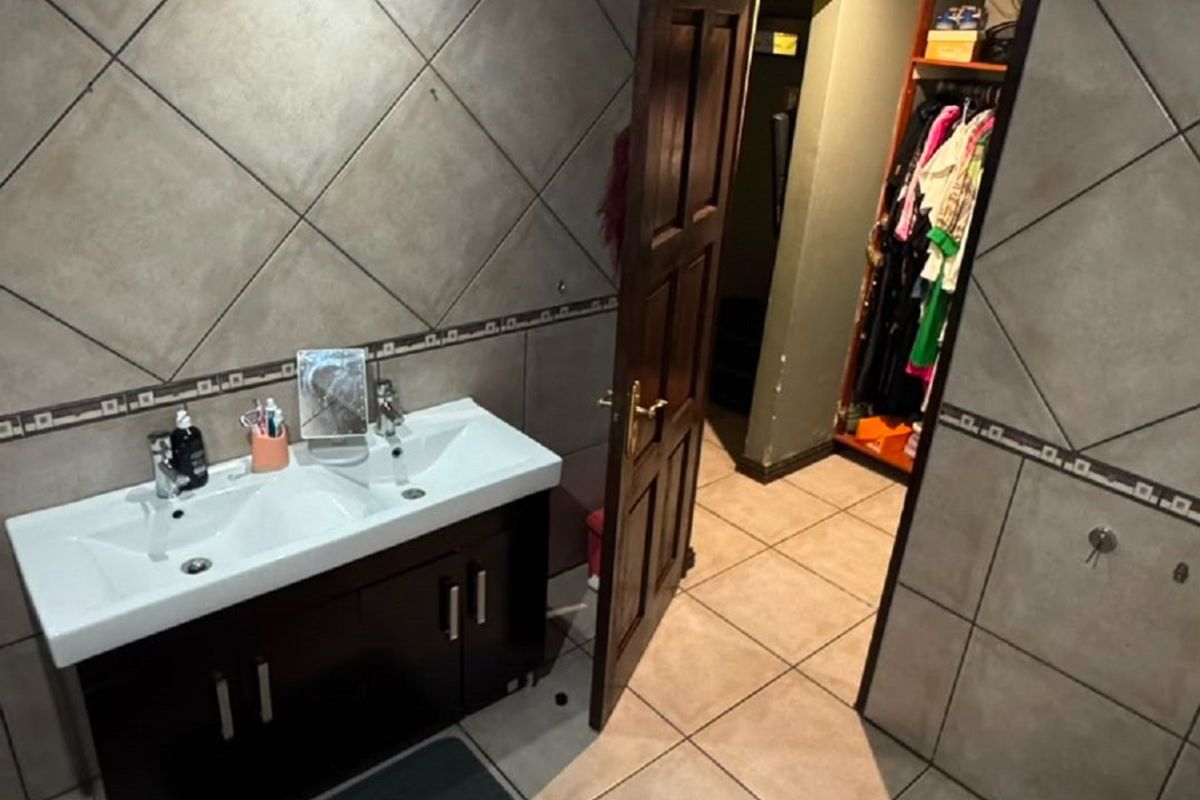 Bathroom featuring a double vanity, jetted bathtub, and tiled finishes, with an adjacent walk-in closet area.