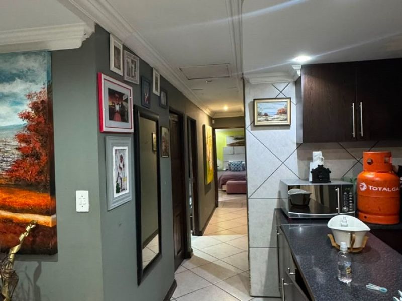 A hallway transition area featuring tiled flooring, decorative ceiling molding, and access to adjacent rooms, including a kitchen area with dark cabinetry.