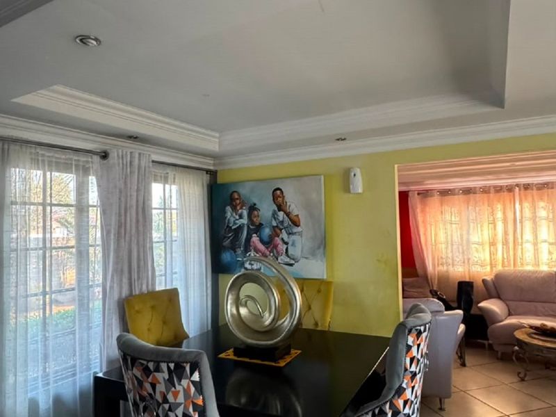 Dining area featuring ceramic floor tiles, recessed ceiling detail, and cove cornicing, with an open-plan flow into the adjacent living space.