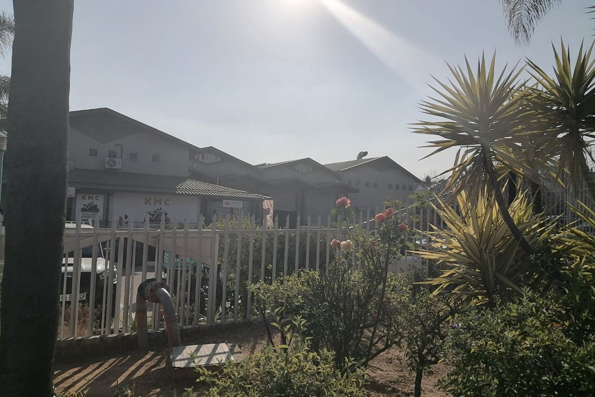 Front view of a commercial property complex featuring pitched roofs, metal perimeter fencing, and established garden landscaping.