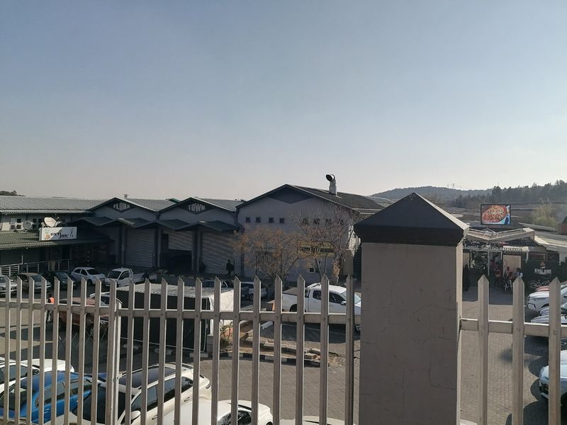 Exterior view of a commercial complex featuring industrial units with roller shutter doors, paved parking, and secure perimeter fencing.