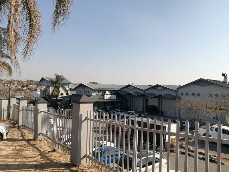 An elevated view of a commercial property complex featuring multiple warehouse units with roller shutter doors, paved parking, and secure perimeter fencing.