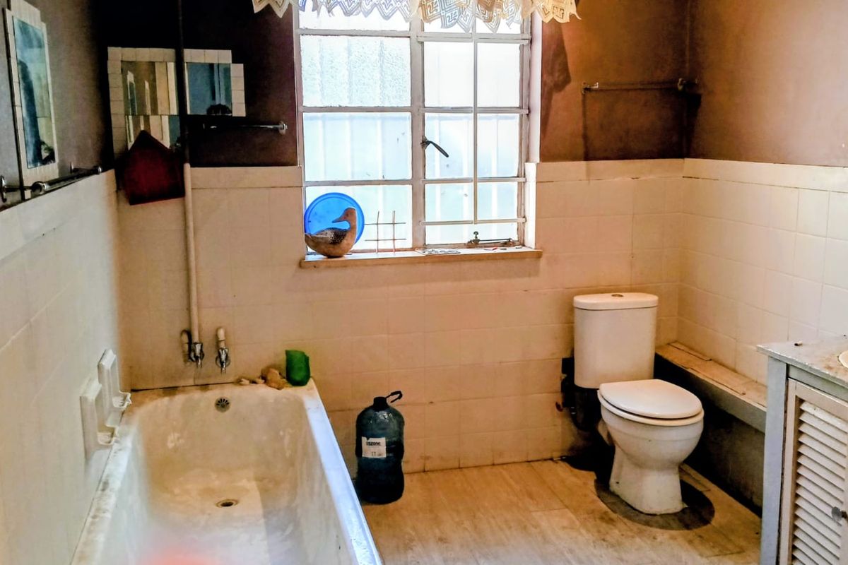 A dated bathroom featuring a standard bathtub, toilet, and vanity unit with tiled walls, requiring modernization and cosmetic updates.