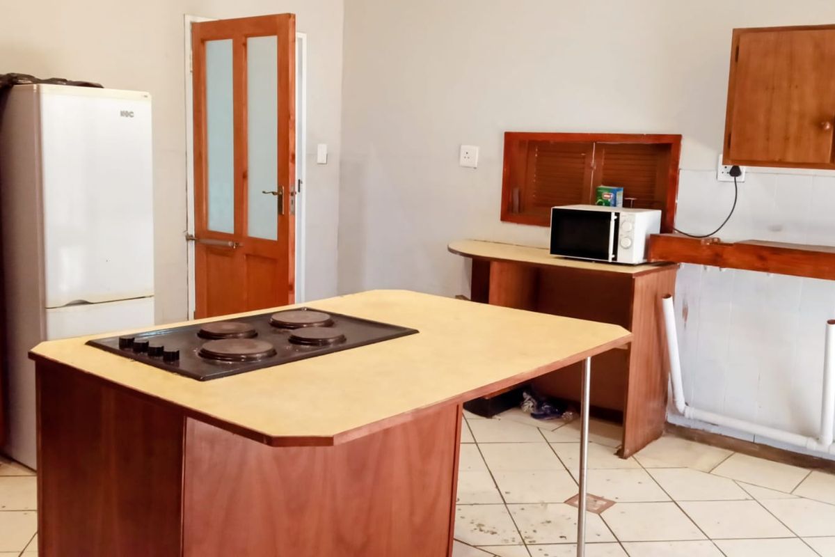 A dated kitchen featuring wooden cabinetry, a central island with a built-in hob, and tiled flooring in need of maintenance.