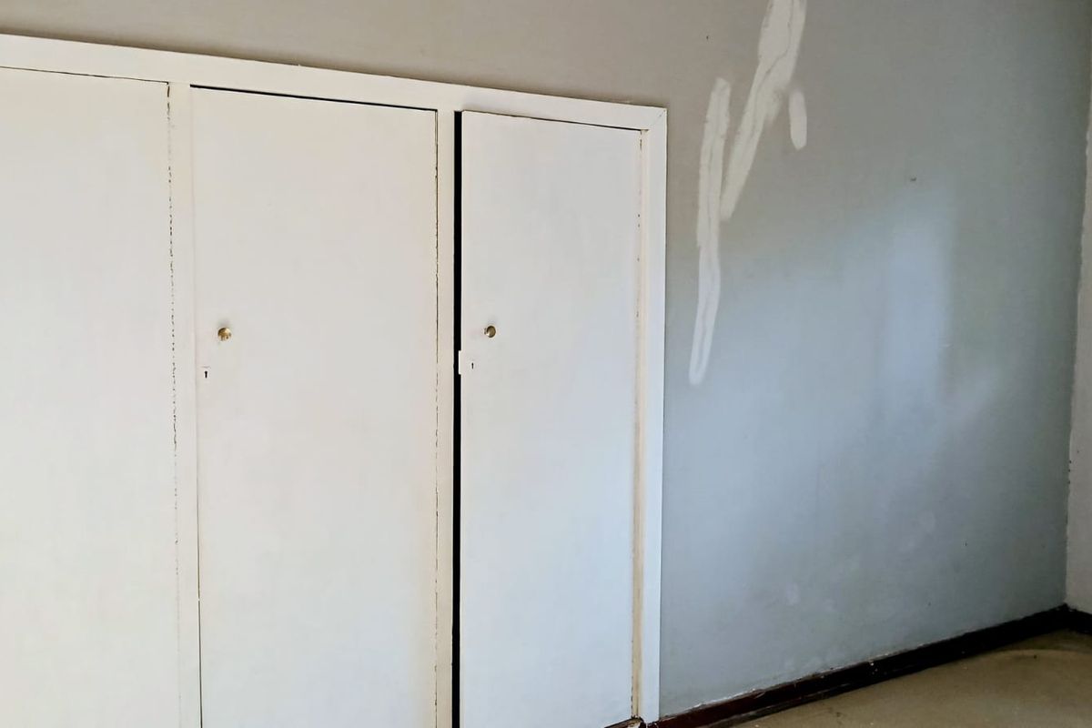 An empty bedroom featuring built-in cupboards, requiring cosmetic attention to the wall surfaces.