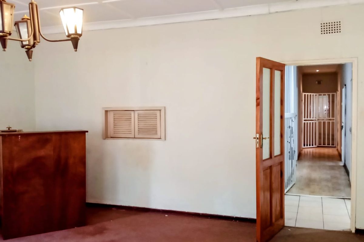 An empty living area featuring a classic chandelier, wooden door, and access to a hallway with security gates.