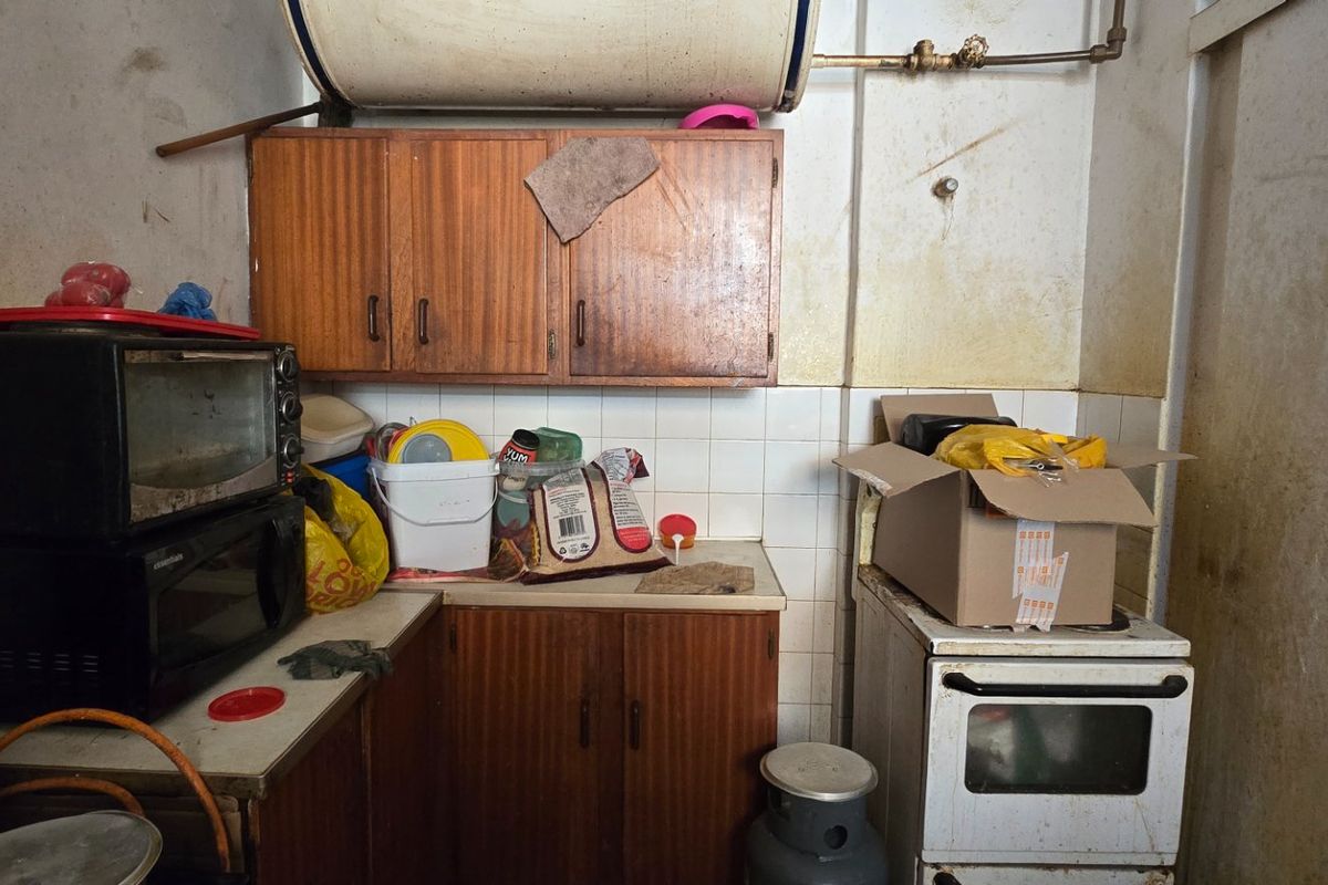 A dated kitchen area featuring original wooden cabinetry, a tiled backsplash, and a freestanding stove, requiring significant refurbishment and cosmetic updates.
