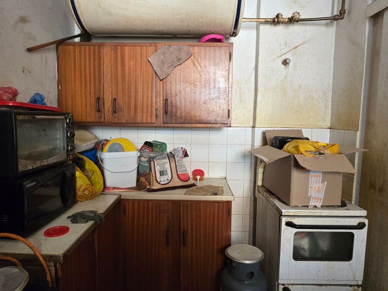 A dated kitchen area featuring original wooden cabinetry, a tiled backsplash, and a freestanding stove, requiring significant refurbishment and cosmetic updates.