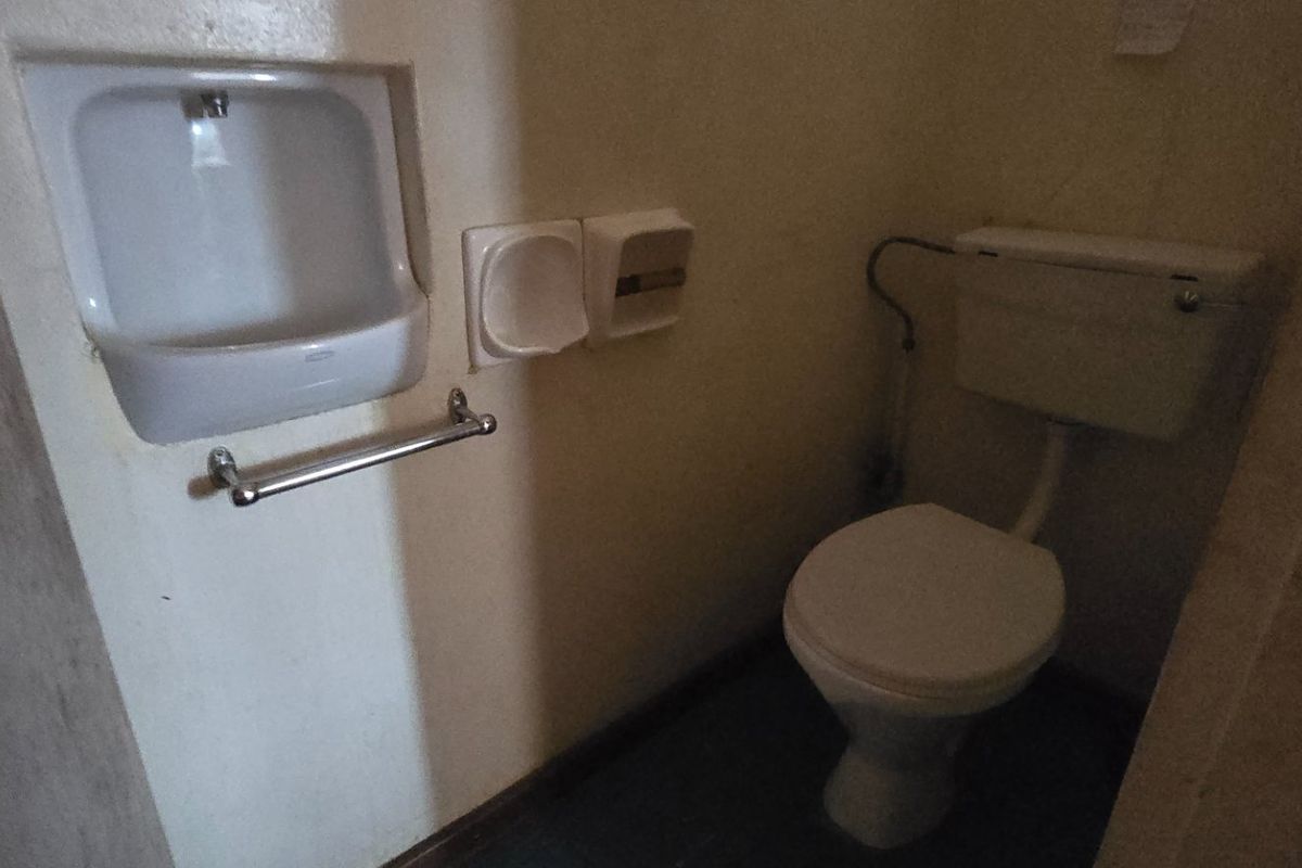 A compact bathroom featuring a standard toilet and a wall-mounted basin, requiring cosmetic updates to improve the overall aesthetic and functionality.