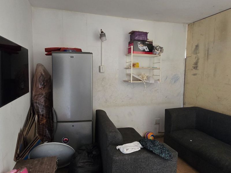 A living room area featuring wall-mounted lighting and electrical outlets, currently requiring significant wall repairs and cosmetic refurbishment to improve the overall condition.