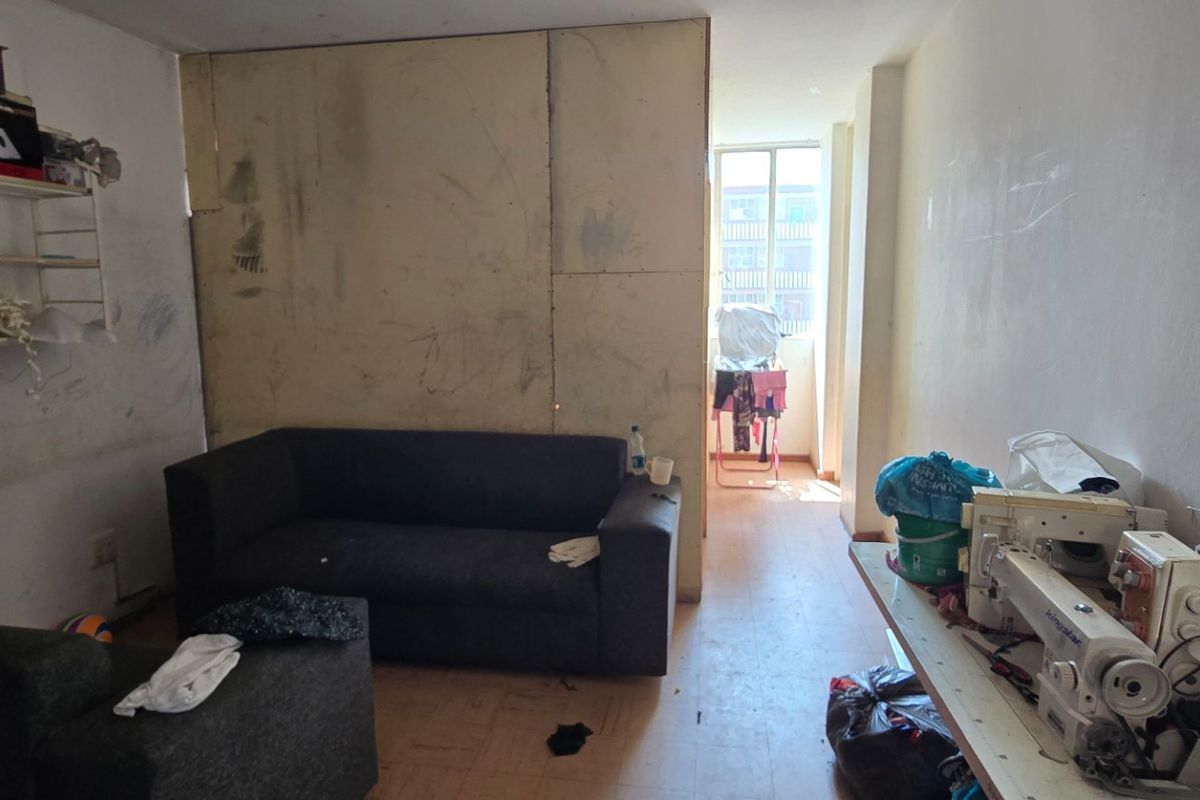 A living room area featuring laminate flooring and a window, currently requiring significant cosmetic repairs and wall refinishing.