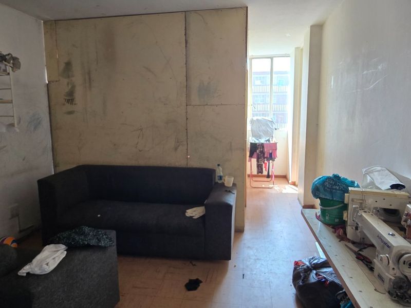 A living room area featuring laminate flooring and a window, currently requiring significant cosmetic repairs and wall refinishing.