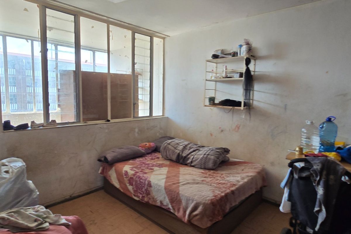 A bedroom featuring a large window and built-in shelving, currently requiring significant cosmetic repairs and wall refurbishment.