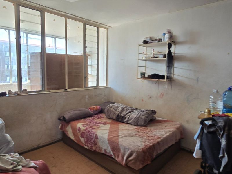 A bedroom featuring a large window and built-in shelving, currently requiring significant cosmetic repairs and wall refurbishment.