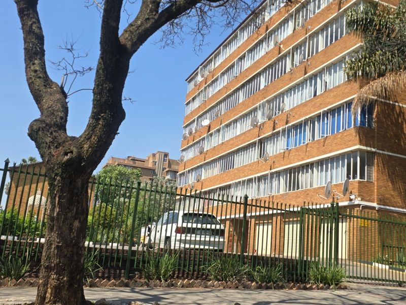 Exterior view of a multi-story brick apartment building featuring large windows and secure perimeter fencing.