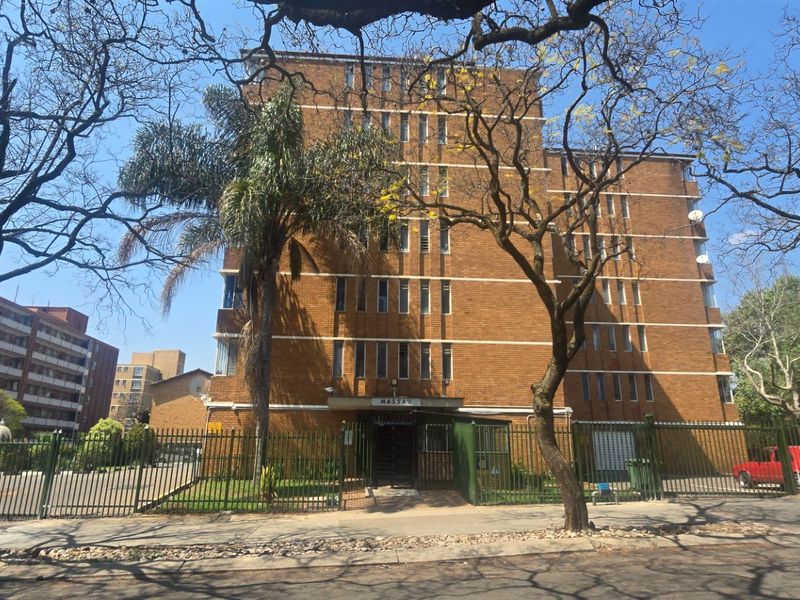 Front elevation of a multi-story brick apartment building featuring secure perimeter fencing and a gated entrance.