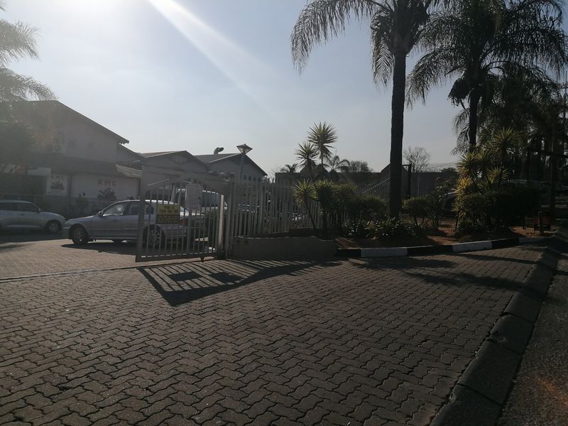 Front entrance view of the commercial property featuring a paved driveway, secure metal gate, and established garden landscaping.