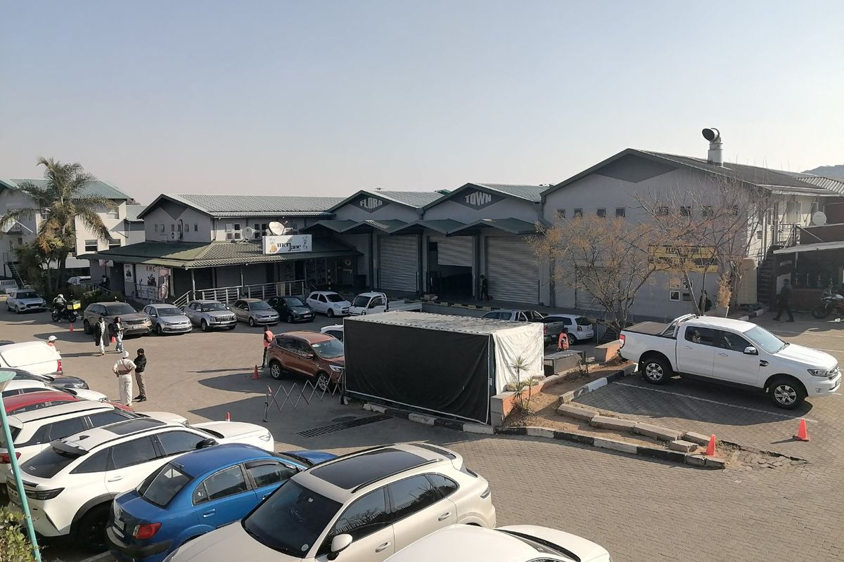 Exterior view of a commercial property complex featuring multiple warehouse-style units with roller shutter doors and an expansive paved parking area.
