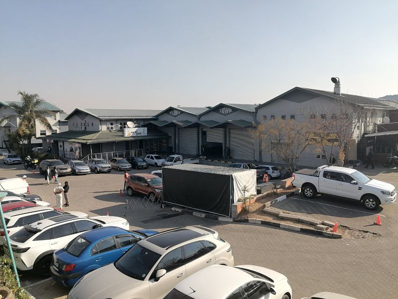 Exterior view of a commercial property complex featuring multiple warehouse-style units with roller shutter doors and an expansive paved parking area.