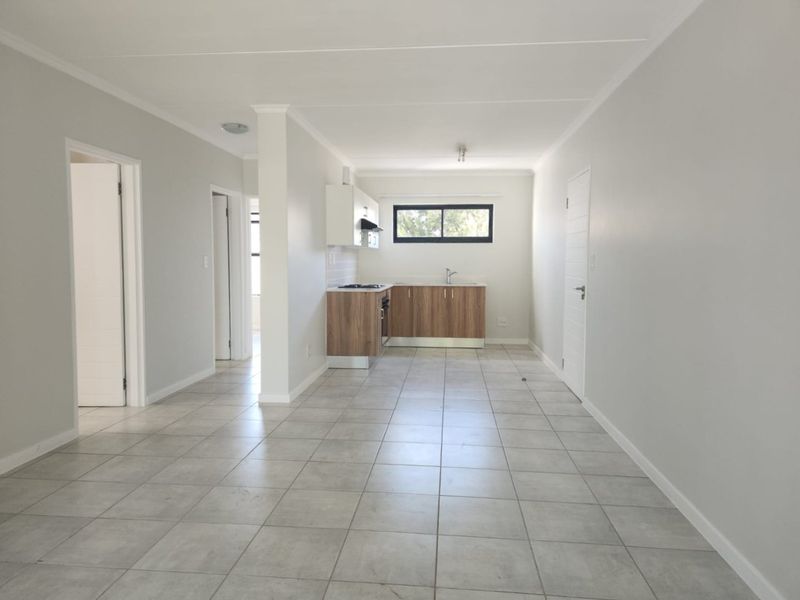 An open-plan living and kitchen area featuring neutral tiled flooring, modern wood-finish cabinetry, and a built-in stove, offering a clean and versatile living space.