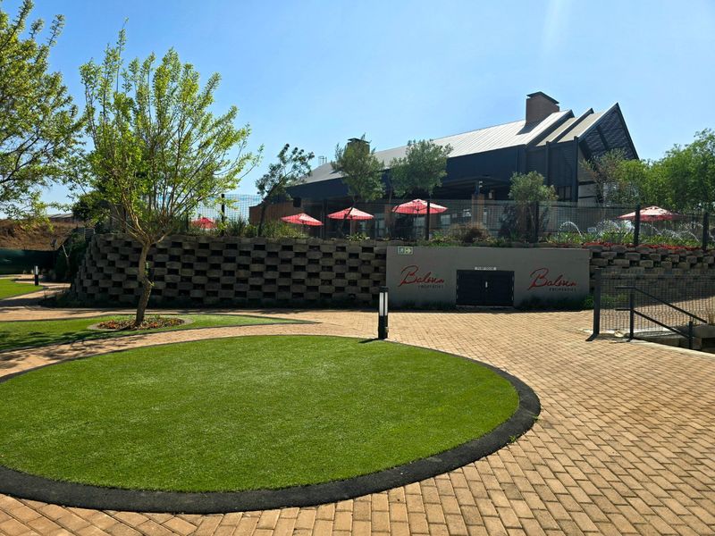 A well-maintained outdoor area featuring a paved courtyard, circular artificial lawn, and a retaining wall leading up to a modern building structure.