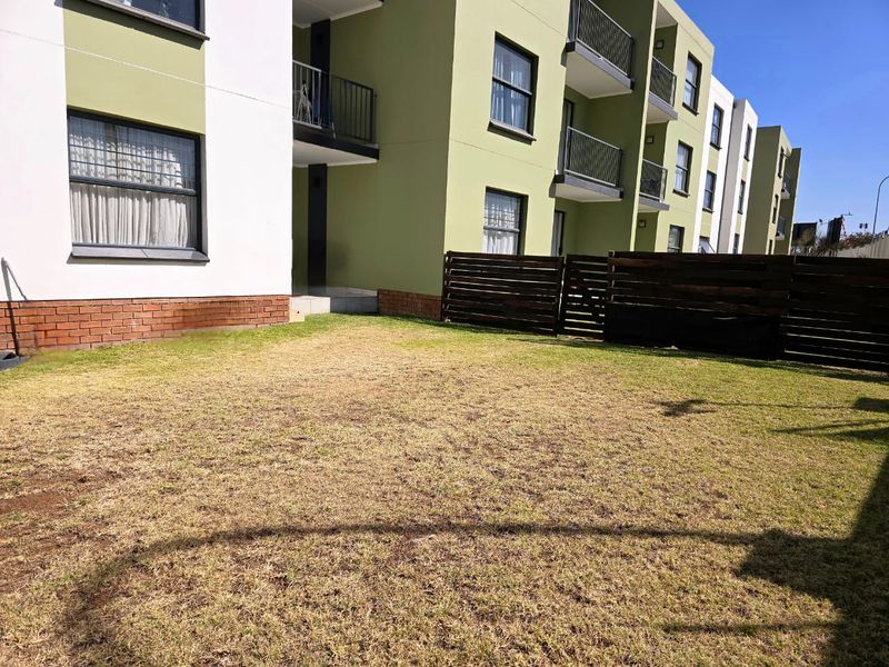 A rear view of an apartment complex featuring a private lawn area, timber fencing, and multi-level balconies with brick and rendered facade finishes.