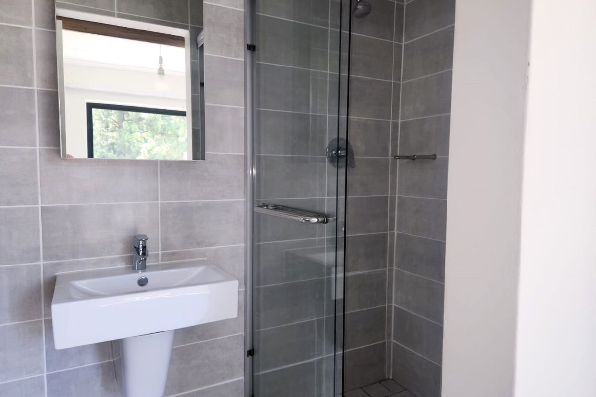 Modern bathroom featuring a pedestal washbasin, chrome fixtures, and a glass-enclosed shower with neutral grey wall tiling.