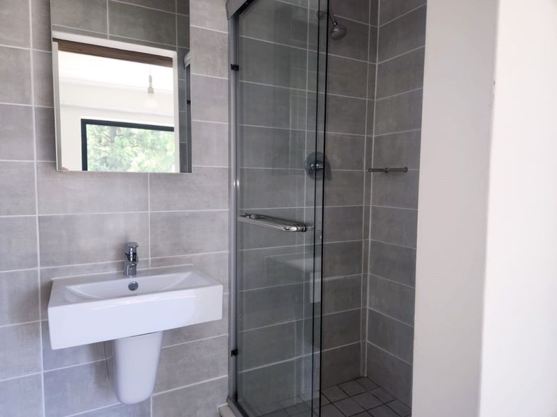 Modern bathroom featuring a pedestal washbasin, chrome fixtures, and a glass-enclosed shower with neutral grey wall tiling.